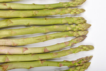 Several fresh green asparagus spears are arranged horizontally on a plain white surface