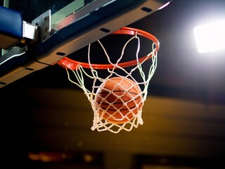 Fototapeta premium A basketball is captured moments from swishing through the hoop in a dynamic indoor court setting.