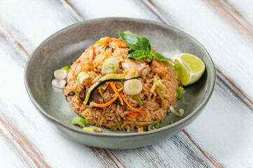 Khao Pad Pet dish with rice, vegetables, chicken and basil, served in a green ceramic bowl on a white wooden background. Bright and inviting photo, perfect for traditional Thai and Asian cuisine theme