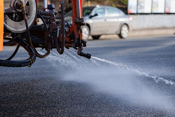 Street cleaning machine spraying water onto asphalt road during daytime, maintaining cleanliness...