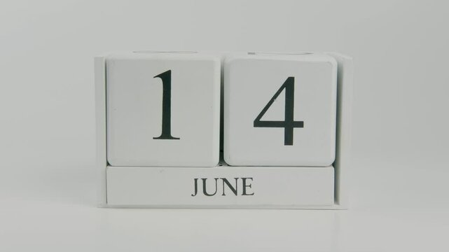 A hand flips a wooden calendar from June 14th to June 15th on a white background, marking the change of date