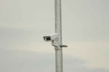 security camera on a metal pole against a cloudy sky