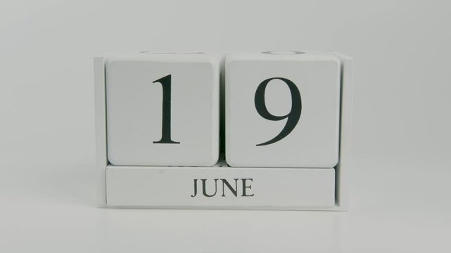 A hand flips a wooden calendar from June 19th to June 20th on a white background, symbolizing the passage of time