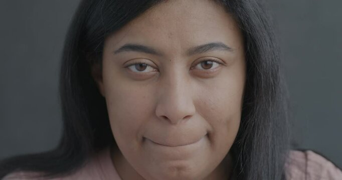 Close-up slow motion portrait of sad young lady looking at camera feeling miserable on black color background. People and negative emotion concept.
