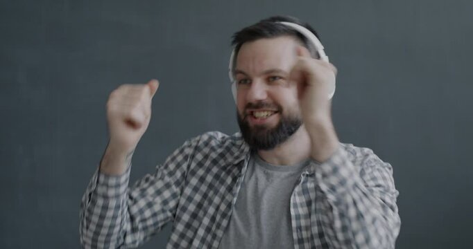 Portrait of joyful person dancing listening to music with headphones having fun on gray color background. Modern technology and entertainment concept.