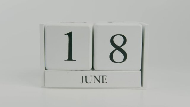 A hand flips a wooden calendar from June 18th to June 19th on a white background, representing the passage of time