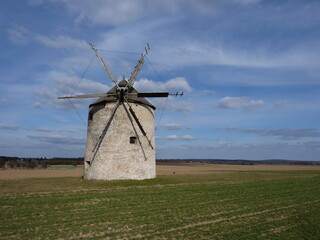 An old windmill photographed from the front next to the March sprouting plowing, with rain clouds in the distance.