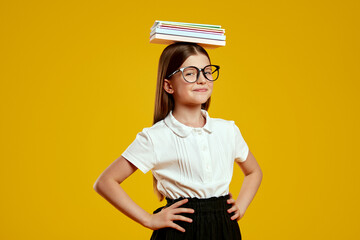 Playful child wearing school uniform and eyeglasses confidently balances books on her head, exuding charm and focus. Ideal for educational campaigns and creative advertising.