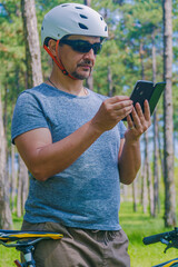 Short Respite: A sport enthusiast paused their bicycle ride to check data on a phone screen amidst the pine trees of an urban park. Photo as part of a series that highlights theme of healthy living.
