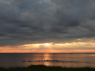 Vibrant, colorful, rays of sunlight, beam down upon the water, from the dark, cloudy, morning sky....