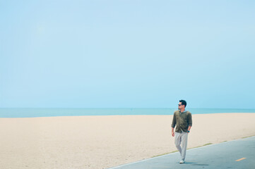 Coastal Stroll: A man strolls along a paved path near a sandy beach, the ocean stretching out before him under a clear sky. The scene evokes feelings of serenity and freedom.