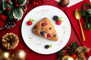 Triangular English scones with blackberries, raspberries and chocolate chips. Top view table with christmas decorations.