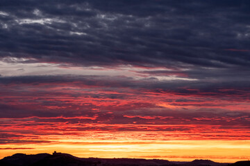 Dramatic sunset with layered clouds over distant horizon, rich in warm and dark hues, conveying serenity, depth and emotional tone for background or inspirational concepts.