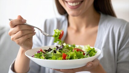 Smiling woman enjoying crisp salad from glass bowl, fork poised mid-bite, sunshine highlighting healthy lifestyle moment.
