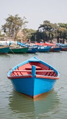 Obraz premium A vibrant blue fishing boat floating calmly on the water, surrounded by other colorful boats.