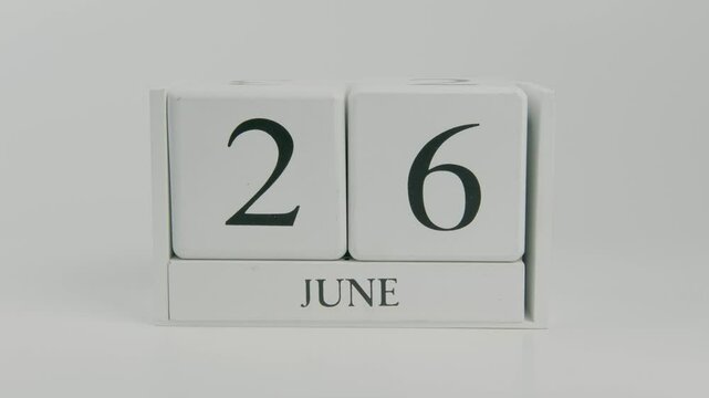 A hand flips a wooden calendar from June 26th to June 27th on a white background, illustrating the passage of time and daily transitions