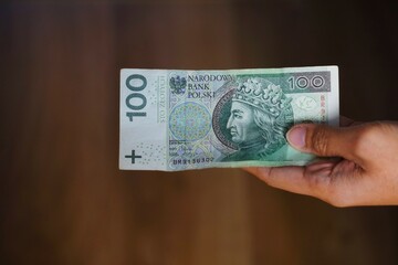 Polski banknot o nominale 100 złotych. Złoty Polski trzymany w dłoni przez kobietę.