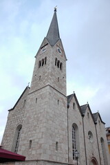 Fototapeta premium Historic stone church with a tall spire under a cloudy sky in a quaint village setting in Europe