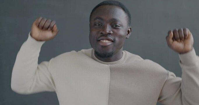 Slow motion portrait of happy African American man dancing looking at camera on gray color background. Entertainment and people concept.