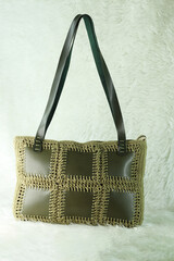 Green shoulder bag knitted using faux leather pieces on a white fluffy blanket. Close-up. Bag crocheted with square motifs. 