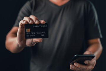 A person in a dark shirt holds a credit card in one hand and a smartphone in the other, representing online payments, digital transactions, financial access, and secure mobile banking solutions.