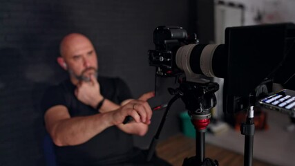Male Caucasian photographer sits looking at the display of camera. Portrait of a cameraman working in studio.