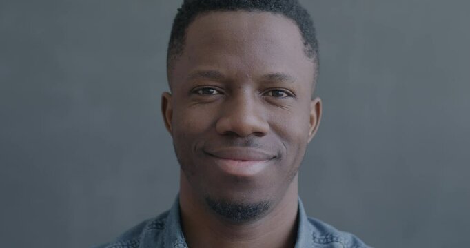 Close-up slow motion portrait of cheerful African American man smiling looking at camera on black color background. People and positive emotion concept.