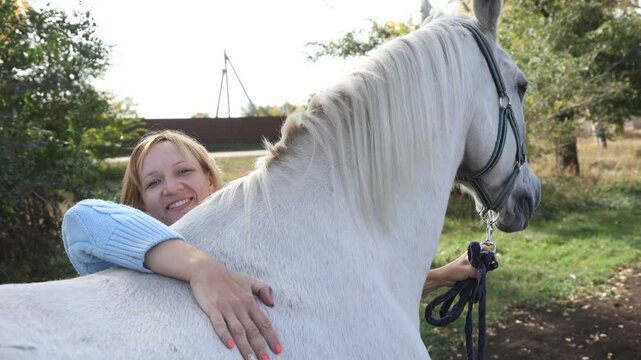 Happy woman pets her horse with love and care. Human and animal friendship concept. High quality 4k footage