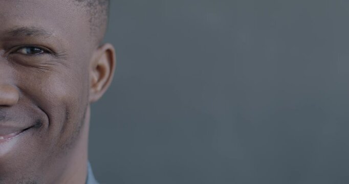 Close-up slow motion portrait of cheerful African American man half face smiling looking at camera on black color background.