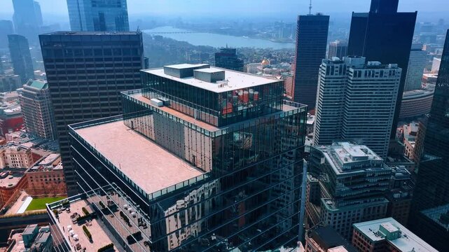 Approaching a few-level glass high-rise building in the downtown of modern city. Drone footage over the smoky panorama of Boston, Massachusetts, USA.