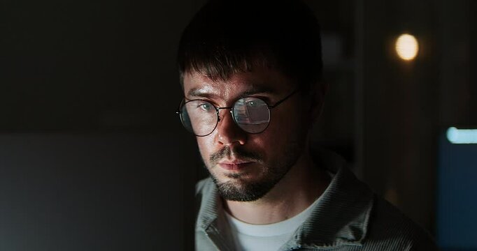 White Caucasian male software developer work late night, program coding in home office. Computer engineering job, data scientist, cybersecurity, information technology. Close-up eyeglasses, handheld