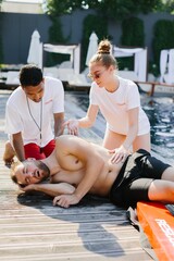 Lifeguards providing first aid to unconscious man at poolside