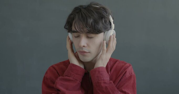 Slow motion portrait of happy young man listening to music with headphones dancing looking at camera on black color background.
