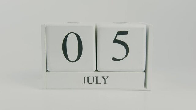 A hand flips a wooden calendar from July 5th to July 6th on a white background, symbolizing the passing of another day