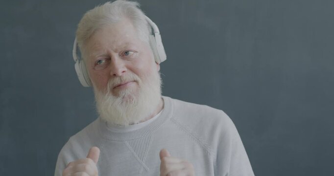 Slow motion portrait of senior man listening to music with headphones and dancing on black color background. Elderly people and fun concept.