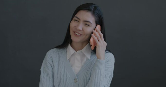 Portrait of cheerful young Asian woman speaking on mobile phone laughing on black color background. People and cellphone communication concept.