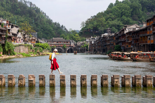 Young tourist dressed in red crossing the Tuojiang River in the historic Xiangxi Phoenix Ancient Town or Fenghuang Ancient Old Town, Hunan, China.