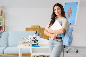 Young female medical student with laptop and backpack at home