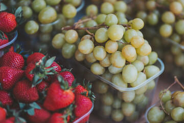 Freshly harvested strawberries and green grapes arranged beautifully at a local market during a vibrant summer day, enticing visitors and shoppers alike