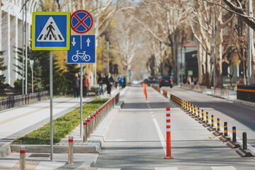 urban street with modern traffic signs and lively pedestrians in a sunny day. Straight two way cycle lane along side an asphalt road in the middle of city. Concept of safe bicycle infrastructure.