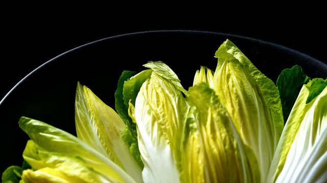 Close-up view of fresh endive heads arranged in a black bowl, showcasing their delicate green and white leaves against a dark background.