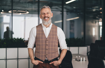 Confident middle-aged Caucasian businessman smiling with hands in pockets, wearing elegant vest and...