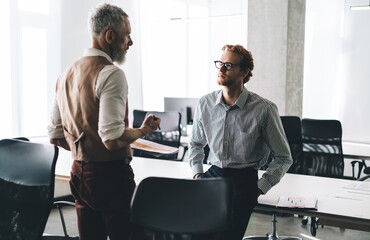 Focused business conversation between senior mentor and young colleague in modern office,...