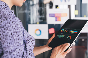 Woman using tablet with dashboard analytics in modern office, focused on screen with colorful...