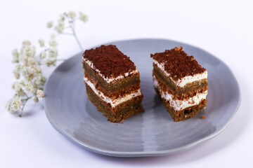 slices of layered cake featuring alternating dark spiced cake layers and creamy white frosting, artfully placed on a round grey ceramic plate. Soft overhead lighting highlights the sharp contrast