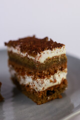 slices of layered cake featuring alternating dark spiced cake layers and creamy white frosting, artfully placed on a round grey ceramic plate. Soft overhead lighting highlights the sharp contrast