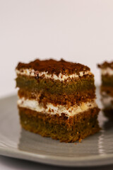 slices of layered cake featuring alternating dark spiced cake layers and creamy white frosting, artfully placed on a round grey ceramic plate. Soft overhead lighting highlights the sharp contrast