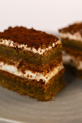 slices of layered cake featuring alternating dark spiced cake layers and creamy white frosting, artfully placed on a round grey ceramic plate. Soft overhead lighting highlights the sharp contrast