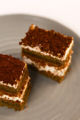 slices of layered cake featuring alternating dark spiced cake layers and creamy white frosting, artfully placed on a round grey ceramic plate. Soft overhead lighting highlights the sharp contrast