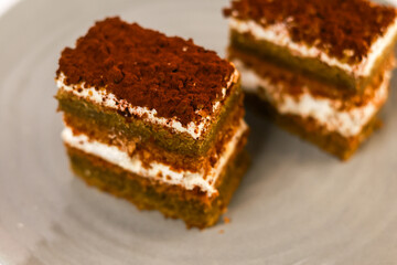 slices of layered cake featuring alternating dark spiced cake layers and creamy white frosting, artfully placed on a round grey ceramic plate. Soft overhead lighting highlights the sharp contrast